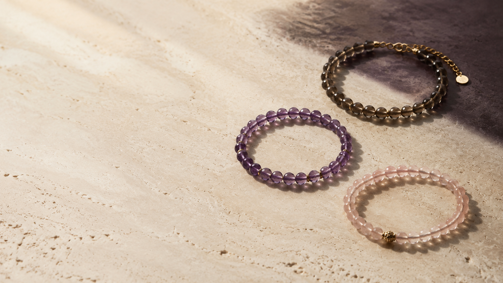 Three crystal bracelets arranged on warm limestone